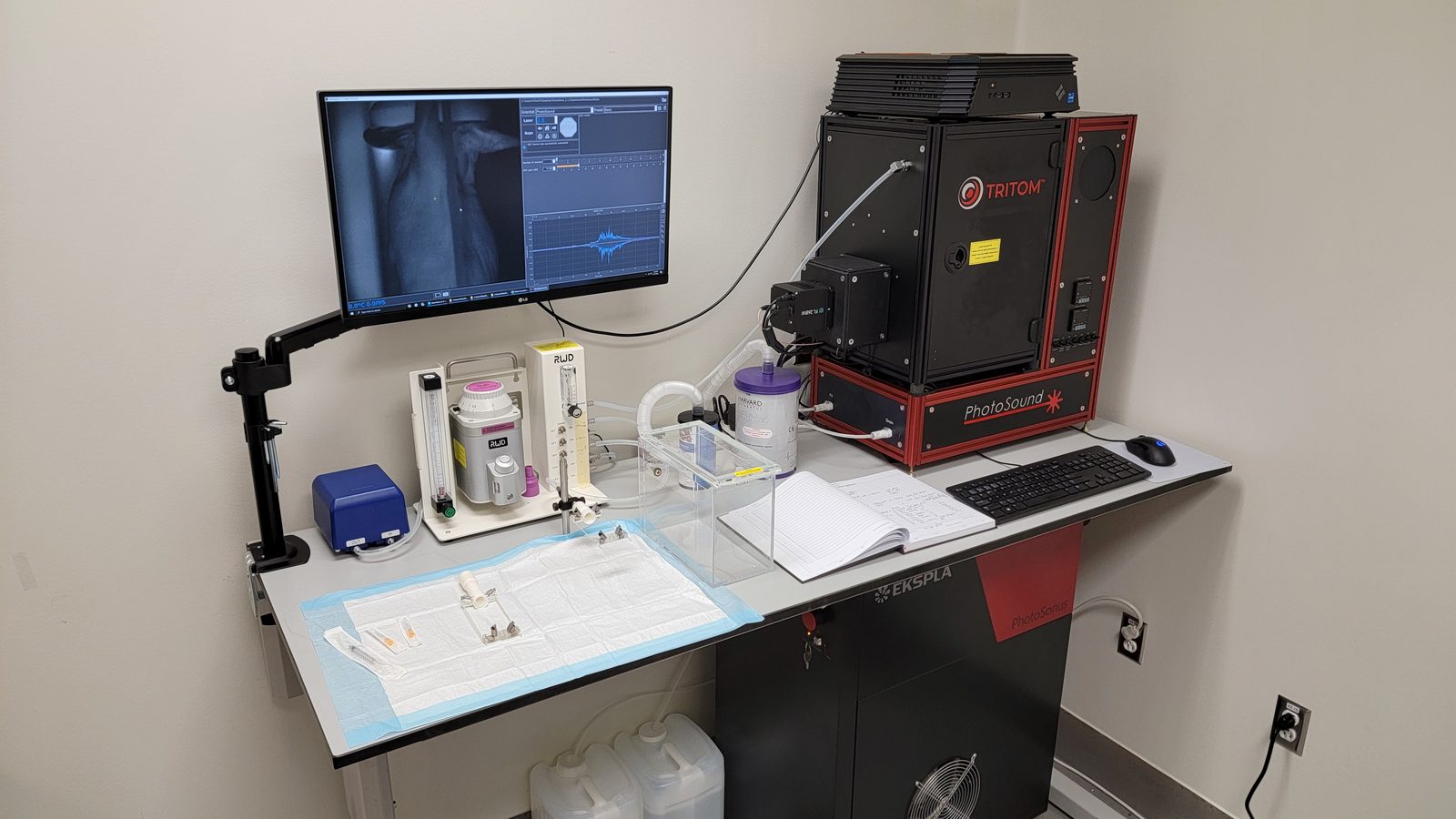 TriTom installed on a laboratory bench next to a monitor showing a reconstructed scan, with the anesthesia system and animal prep area alongside